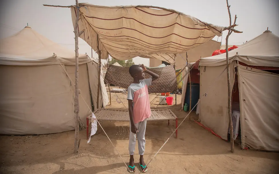 Sudan ist von der größten Kinder-Flüchtlingskrise weltweit betroffen | © UNICEF/UNI623923/Elfatih Ein Junge steht vor einem Zelt und schaut in die Luft
