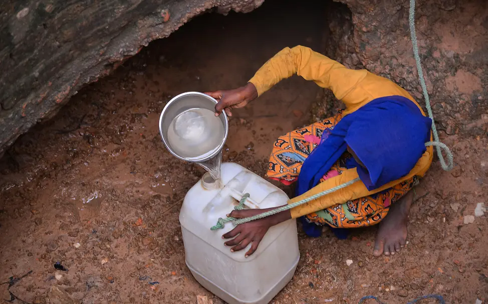Dürre und Wassermangel im Sudan sind ein großes Problem | © UNICEF/UNI578427/Khalil Ein junges Mädchen sitzt in einem trockenen Brunnen und schüttet ein wenig Wasser in einen Plastikkanister