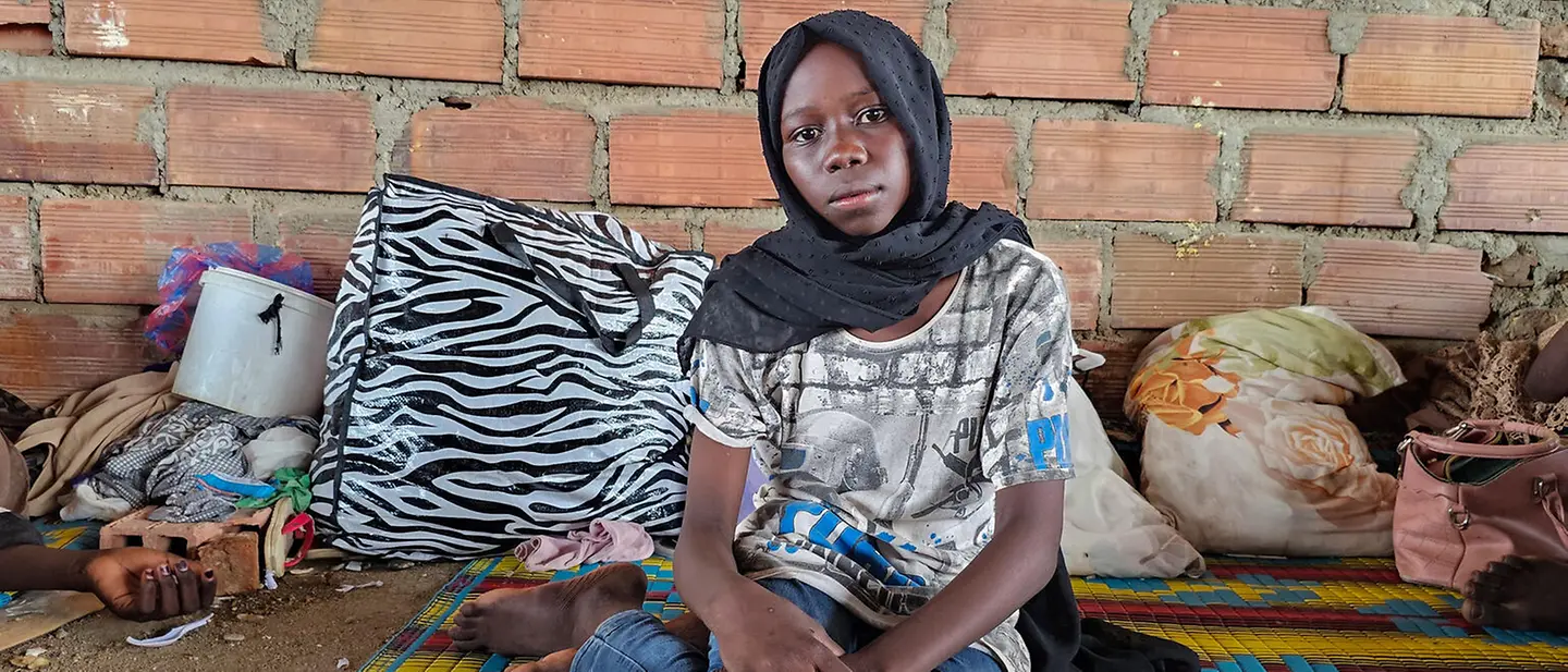 Ein Mädchen aus dem Sudan in einer Geflüchtenunterkunft | UNICEF/UNI611447/Rajab Ein Mädchen sitzt auf einer bunten Matte auf dem Boden